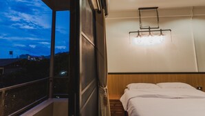 A hotel room with a bed, a nightstand, a hanging light fixture, and a view of the sky. - No.9 Hostel (Chiang Mai)
