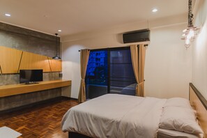 Ein Schlafzimmer mit einem Bett, einem Fernseher auf einer Holzkonsole und einem Fenster mit Vorhängen.