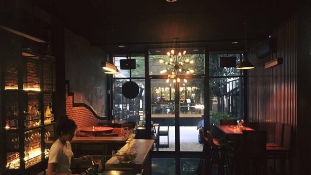 A dimly lit restaurant with a bar area, large windows, and a modern chandelier. - No.9 Hostel (Chiang Mai)