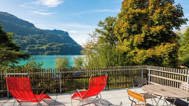 Una terraza con mobiliario exterior, una valla de madera y vistas a un lago y montañas.