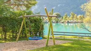Un parque infantil con columpios y un conjunto de columpios, rodeado de árboles y un lago.