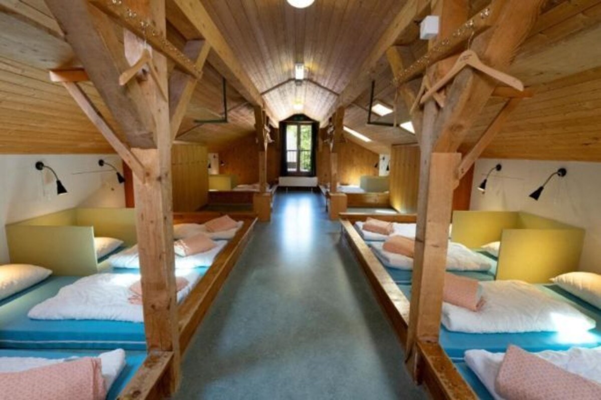 Un pasillo con camas de madera dispuestas a ambos lados, que conduce a una puerta central.