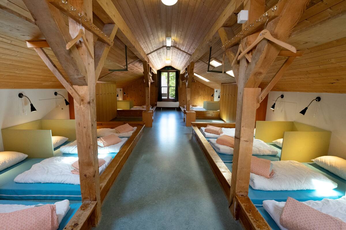 A corridor with wooden beds on either side, a central walkway, and a view of the outdoors through a door at the end.
