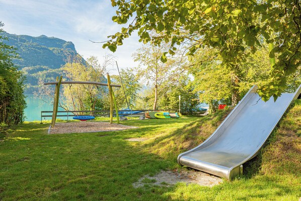 Un parque infantil con tobogán, columpios y vistas a un lago y montañas.