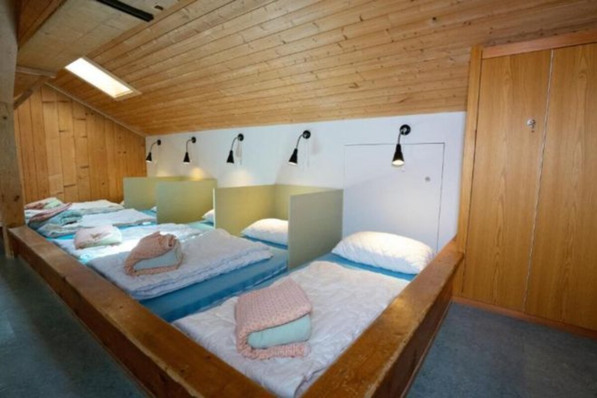 Habitación con paneles de madera y literas, cada una con almohada y manta.