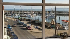 Puerto deportivo con barcos amarrados, una carretera con coches estacionados y un cielo despejado.