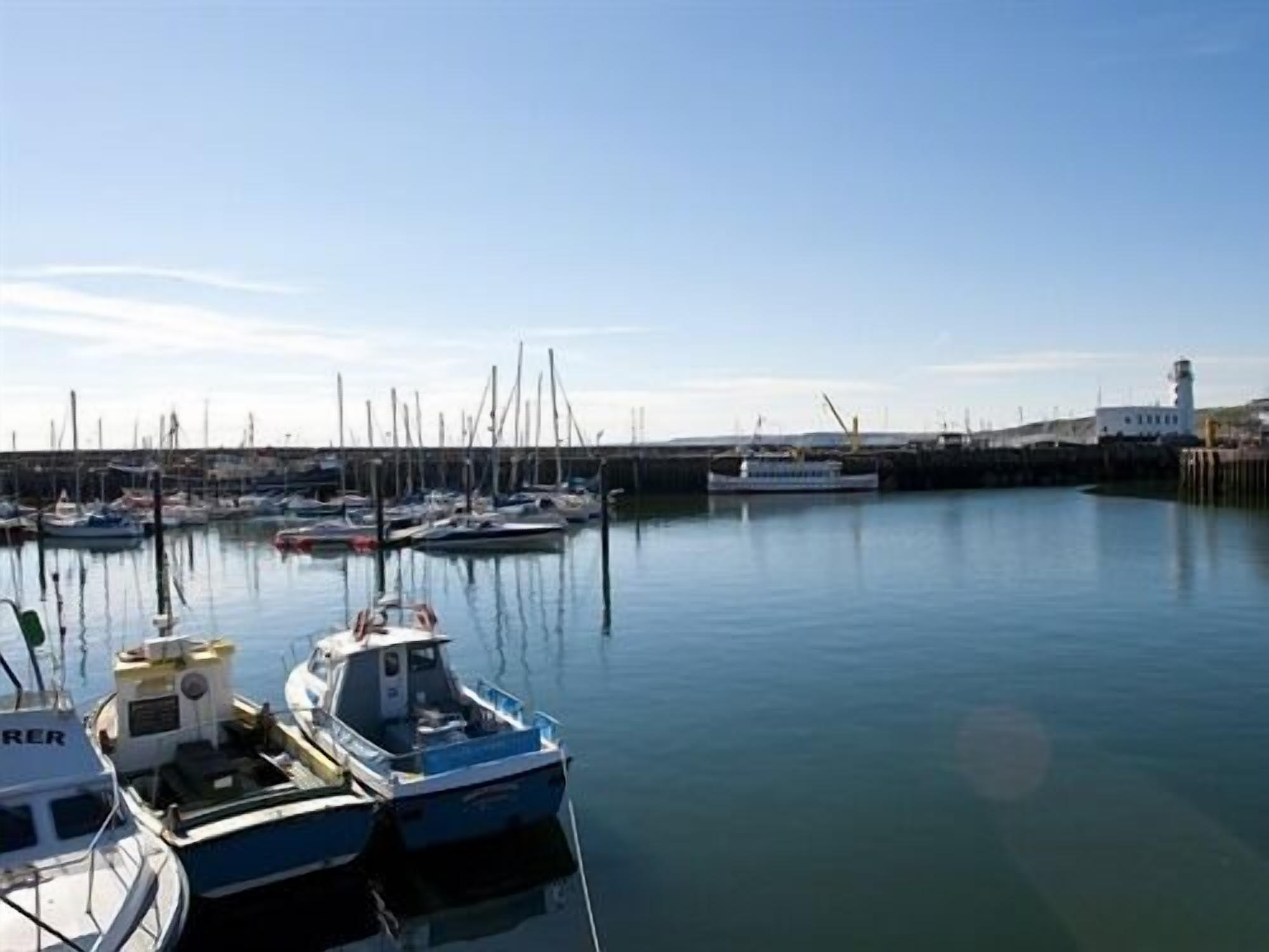 A marina with several boats docked, a lighthouse in the background, and calm water.