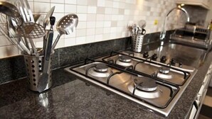 Una cocina con estufa a gas, utensilios de acero inoxidable y salpicadero de azulejos.