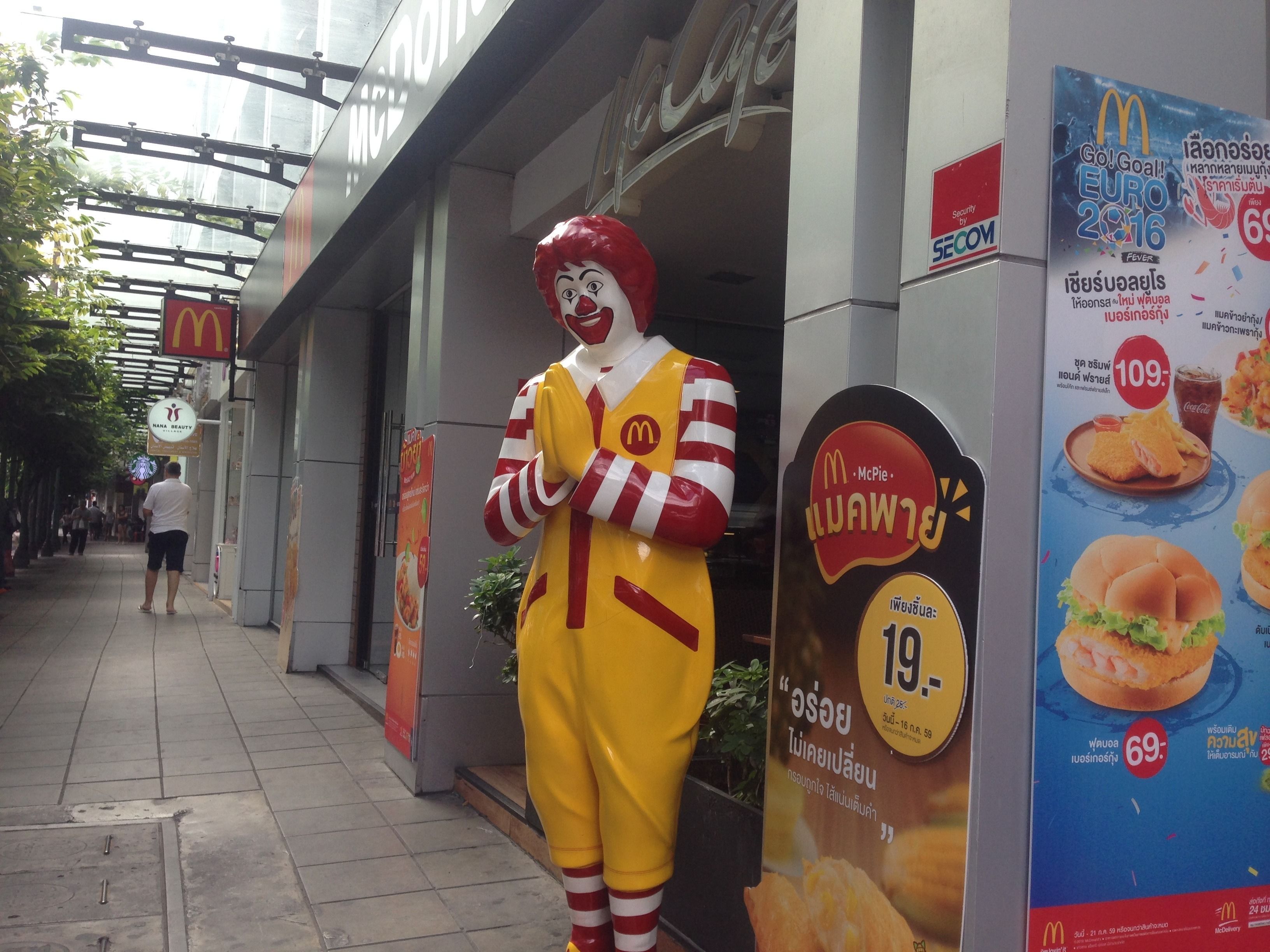 A McDonald's mascot outside a building with a signboard advertising a special offer.