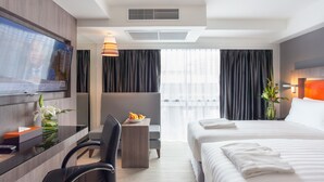 A modern hotel room with a large bed, a desk with a TV, a small table with a vase of flowers, and a seating area with a chair and a sofa. - Grand 5 Hotel & Plaza Sukhumvit Bangkok (Bangkok)