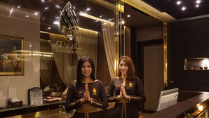 Two receptionists in a modern lobby with a chandelier, a leather sofa, and a reception desk. - Grand 5 Hotel & Plaza Sukhumvit Bangkok (Bangkok)
