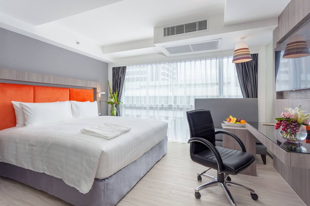 Une chambre d’hôtel moderne, dotée d’un grand lit, d’un bureau avec une chaise, d’une télévision et d’une fenêtre avec des rideaux.