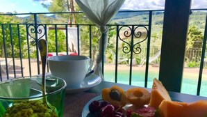 Un balcon avec une table préparée pour le petit-déjeuner, comprenant une assiette de fruits et un verre de jus, donnant sur un paysage magnifique.