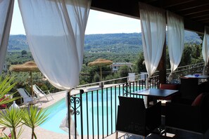 A poolside area with a view of a mountainous landscape, outdoor seating, and a covered section with white curtains. - Borgo del Nespolo (Peschici)