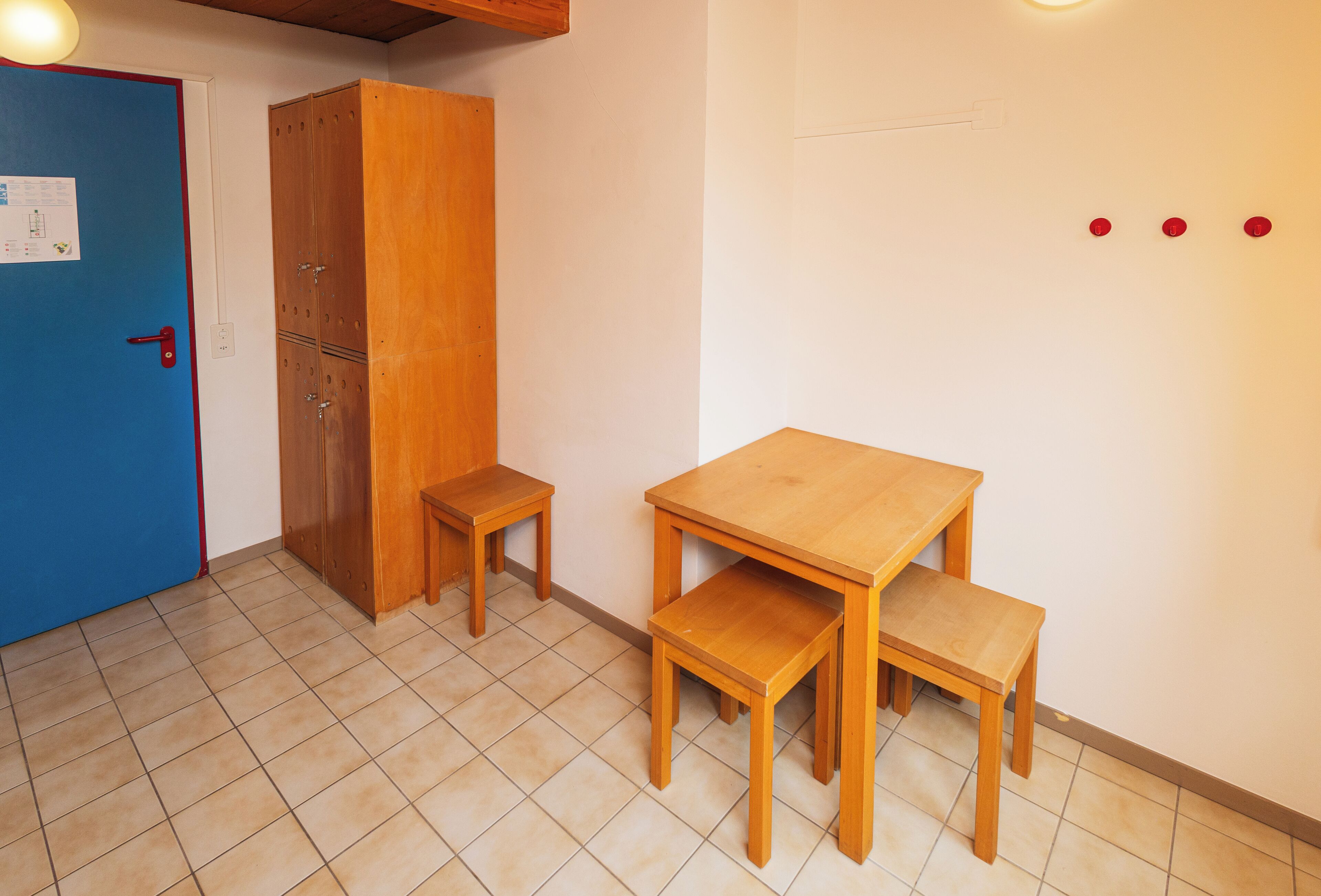 Una habitación con puerta azul, armario de madera y una mesa de madera con dos bancos.