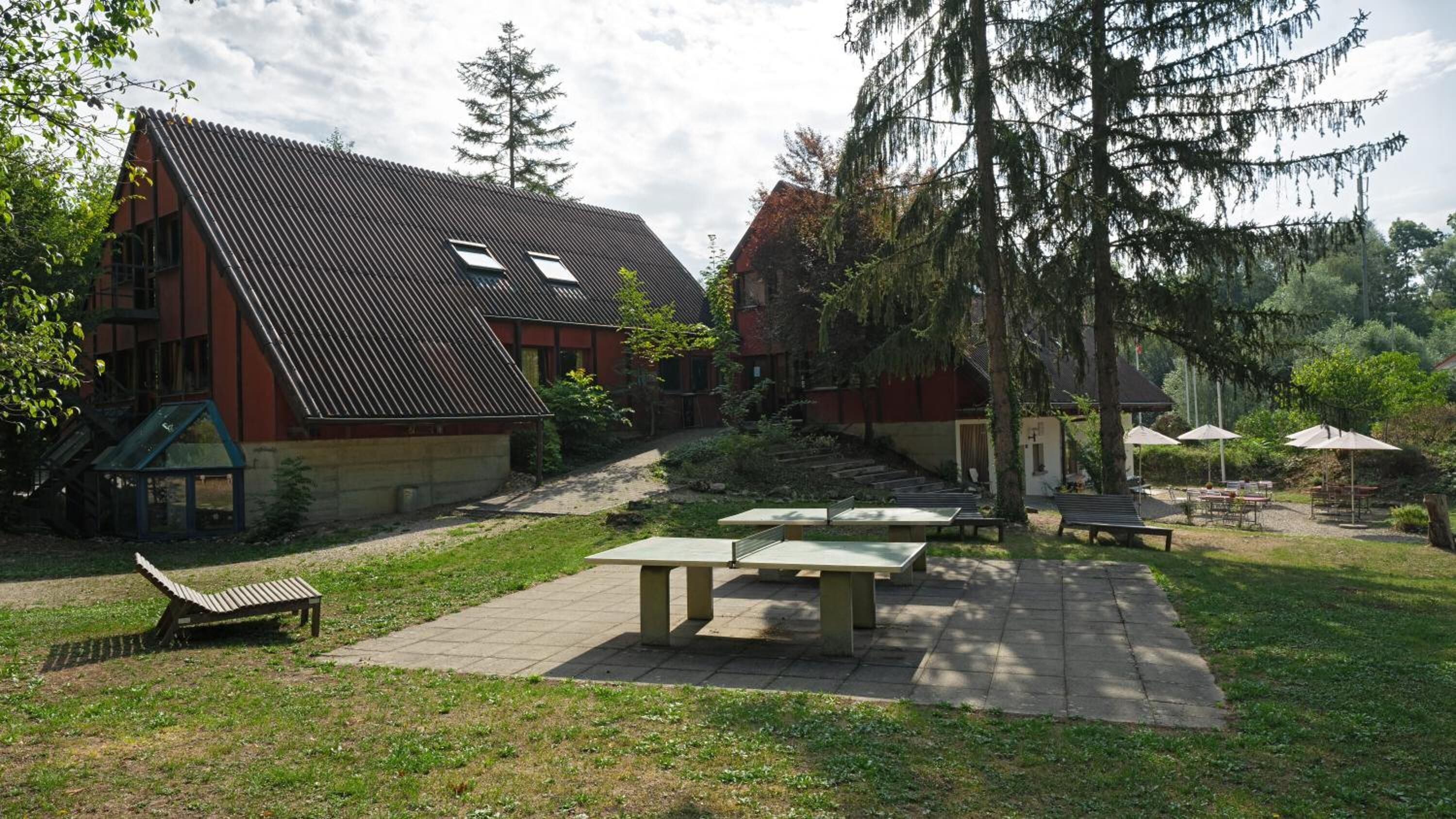 Une cour avec des tables de pique-nique, un banc et un bâtiment doté d’un toit en pente.