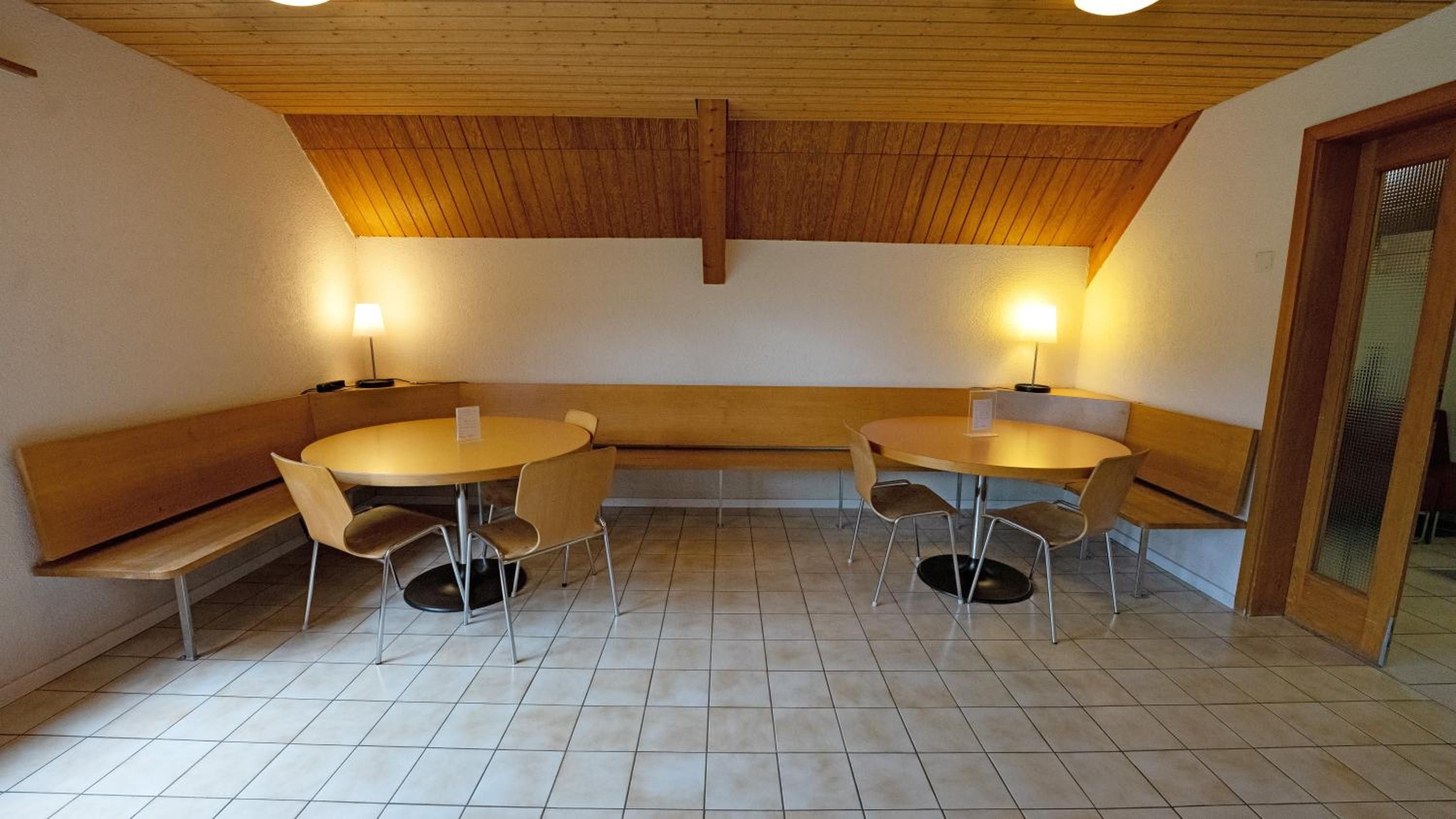 Een kamer met een houten plafond, twee ronde tafels met stoelen, een bank en een deur.