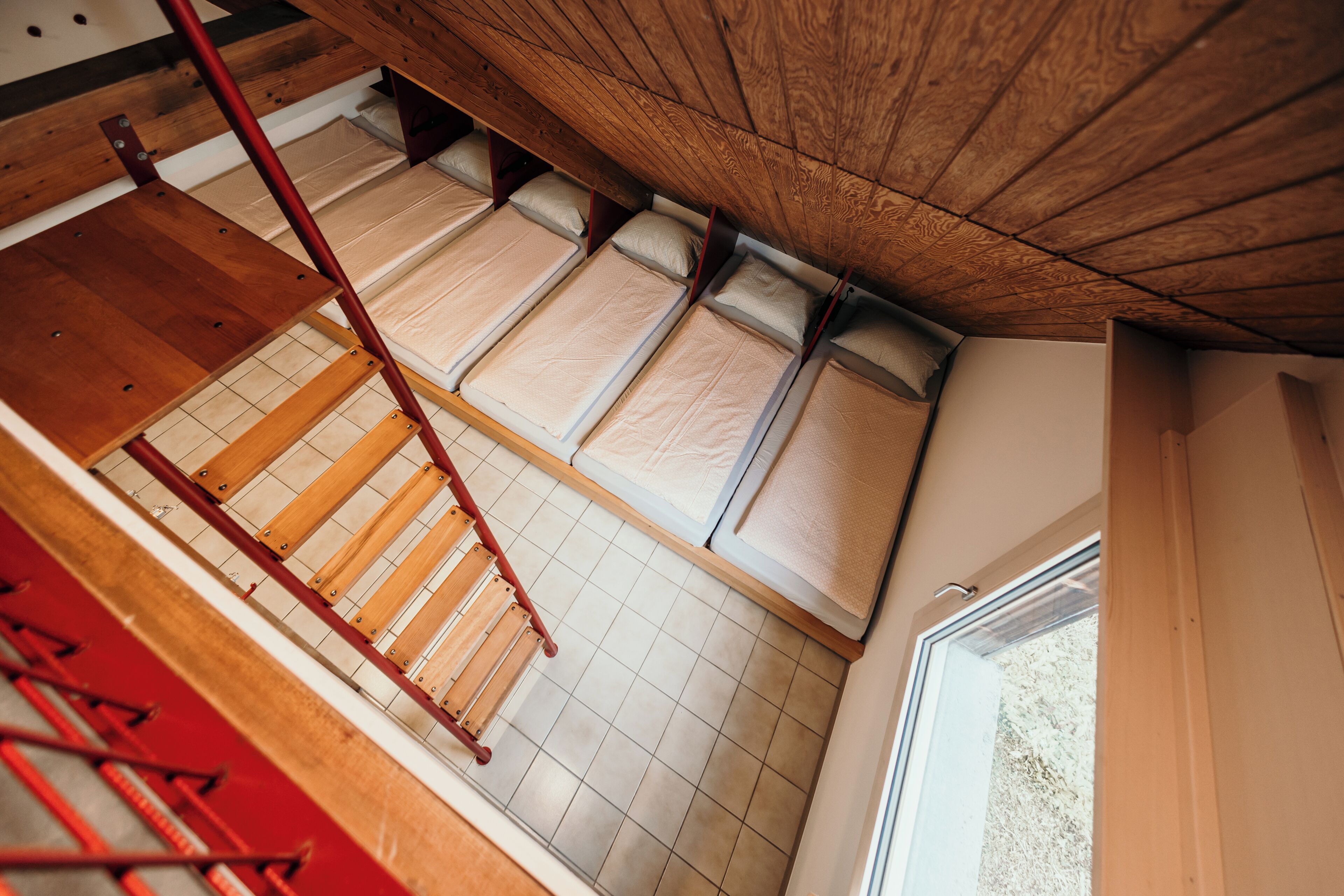 Une chambre de type dortoir, avec des lits superposés, une échelle en bois et une fenêtre.