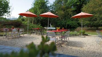 An outdoor seating area with tables and chairs, red umbrellas, and potted plants.