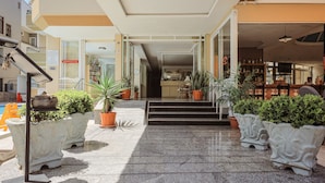 Een hotelentree met een betegelde vloer, potplanten en een trap die naar binnen leidt.