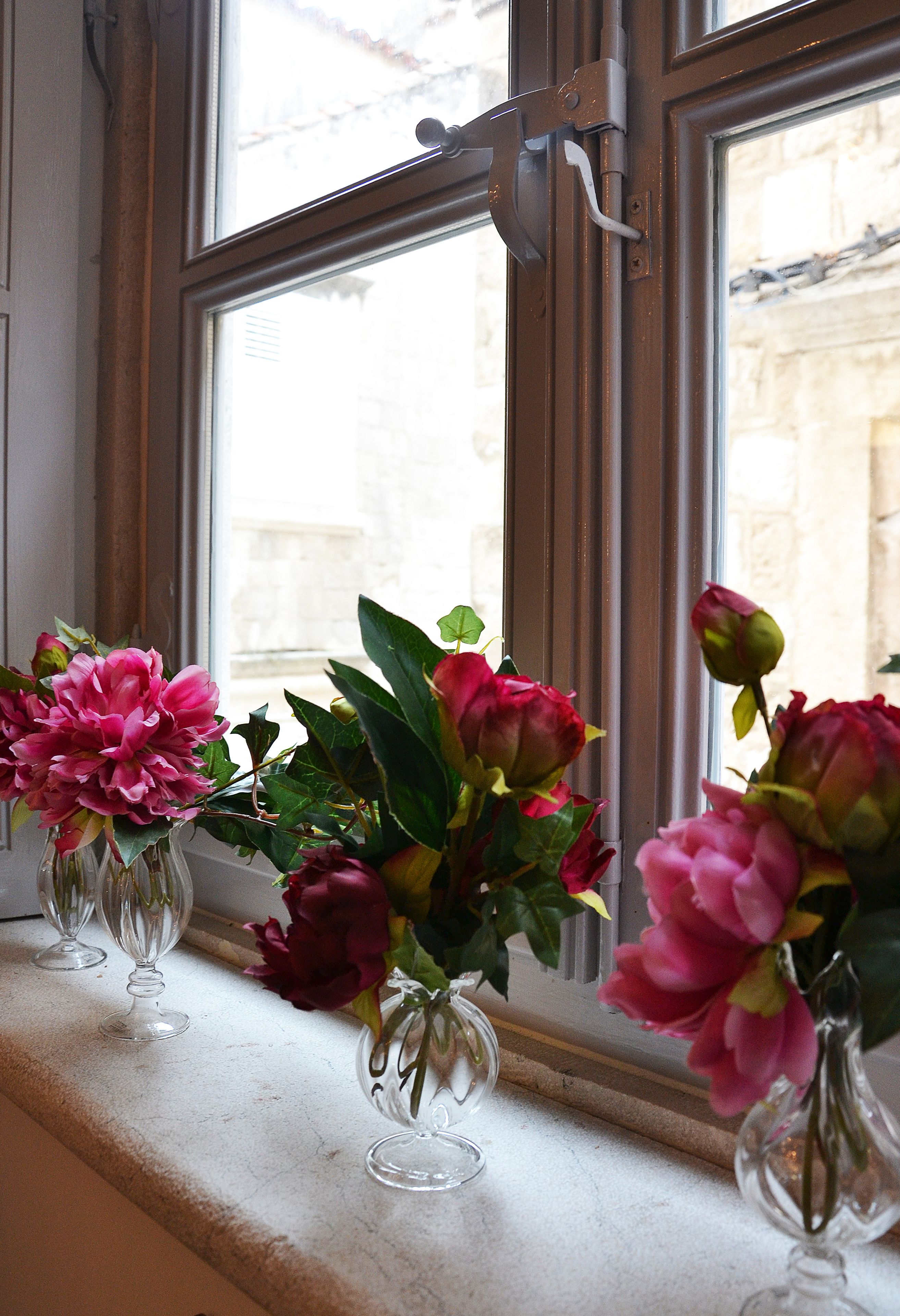 Trois vases ornés de fleurs sont posés sur un rebord de fenêtre.