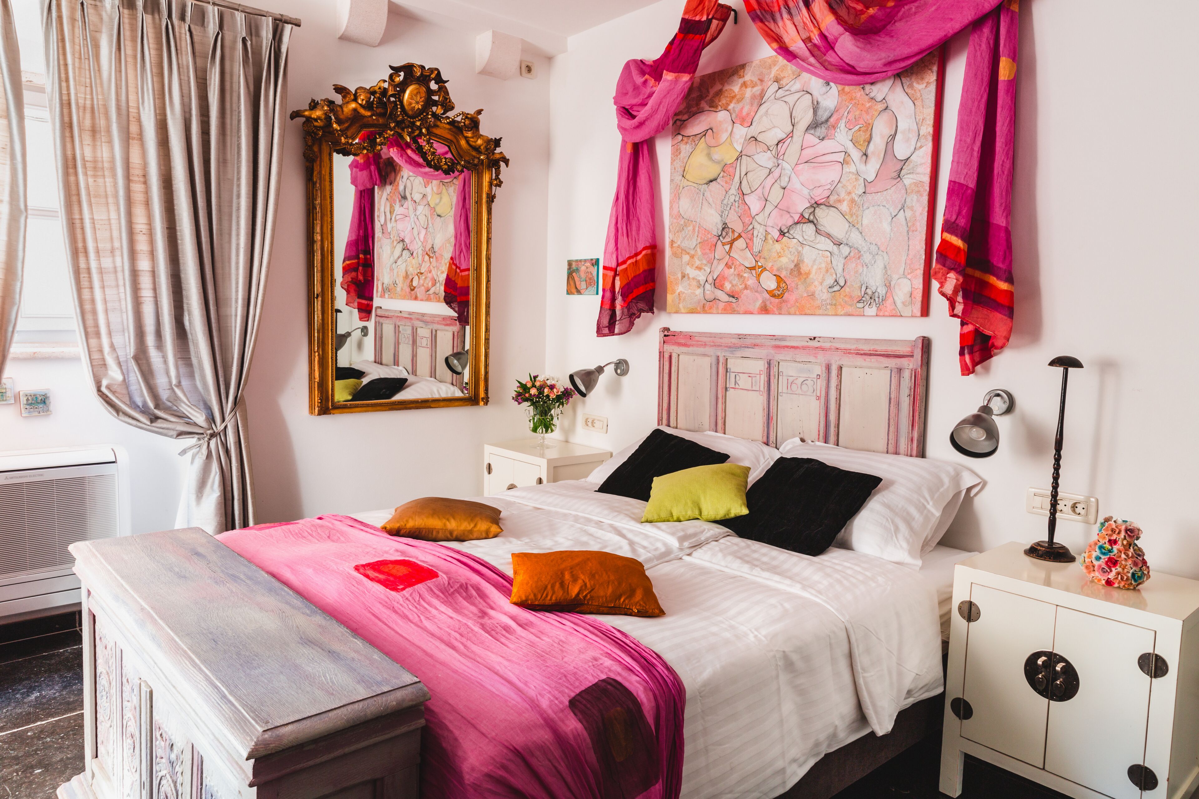 Una camera da letto con un letto, comodini, uno specchio e una finestra con tende.