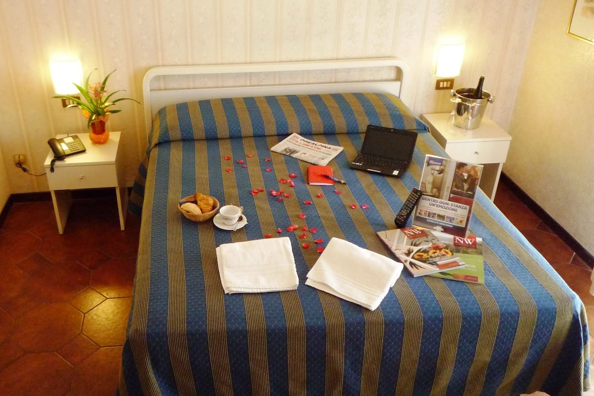 A neatly made bed with a striped bedspread, a laptop, a remote control, a magazine, and a bowl of croissants on the bed.