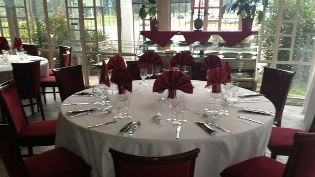 A round dining table with red chairs, set with white tablecloths and red napkins. - Hotel Montecarlo (Castellanza)