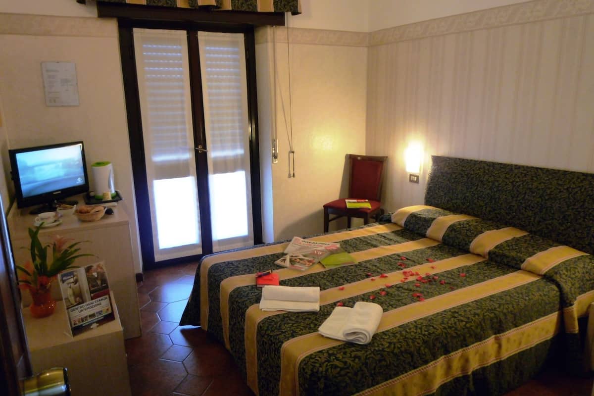 A hotel room with two beds, a television, a small table with a coffee maker, and a door with a view.