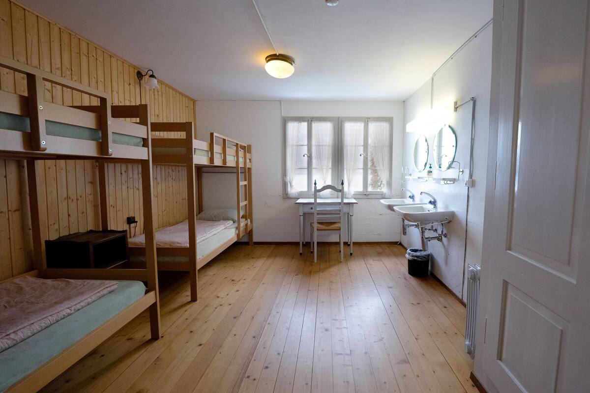 Ein Zimmer mit Stockbetten, einem Schreibtisch, einem Stuhl, einem Waschbecken und einem Spiegel.
