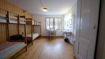 A room with bunk beds, a desk, a chair, a sink, and a mirror.
