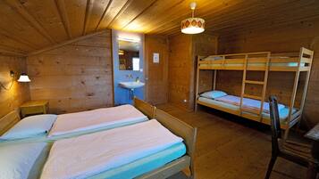 A wooden cabin room with bunk beds, a small bedside table, a sink, and a hanging light fixture.
