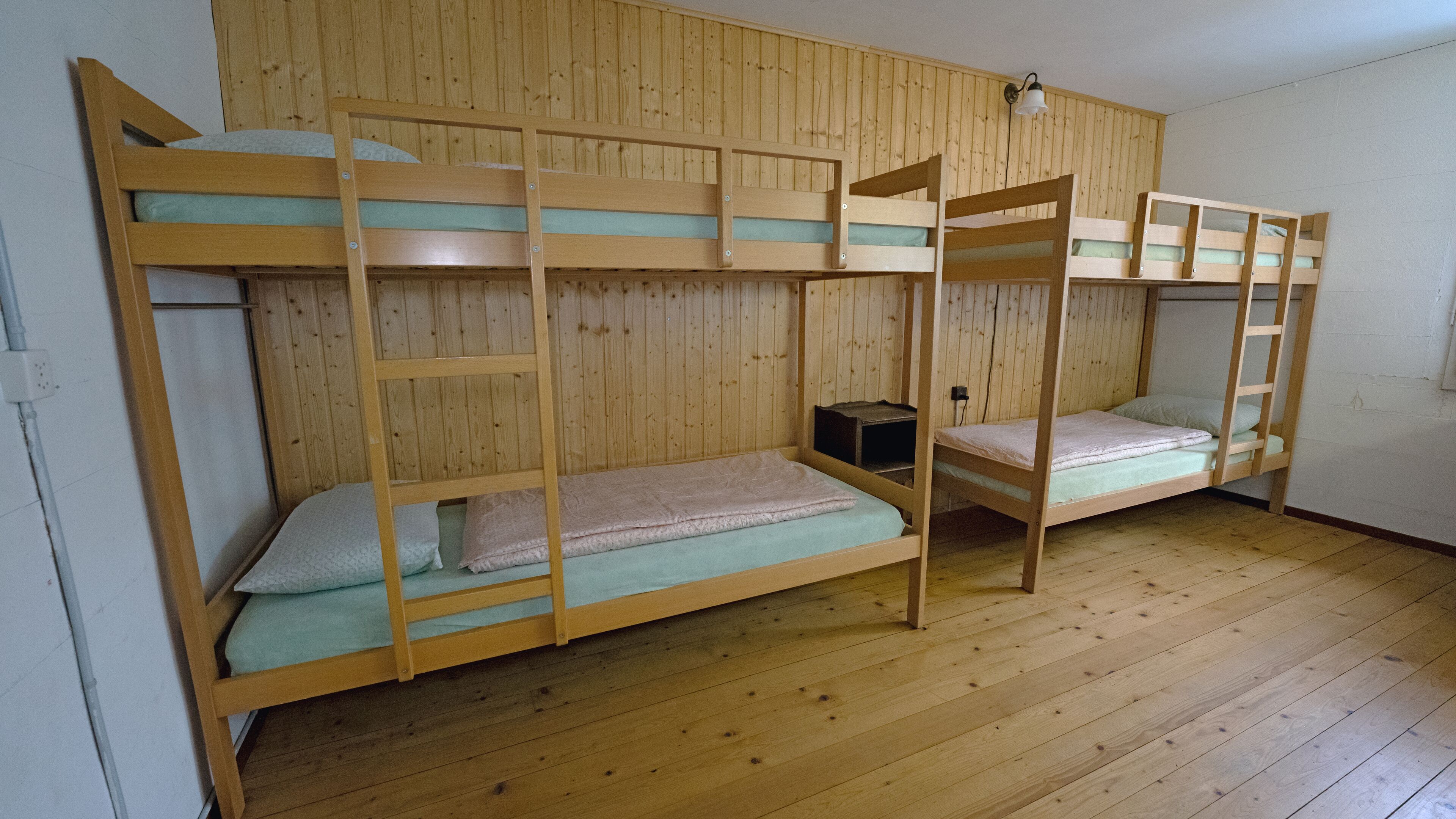 A room with bunk beds, wooden walls, and a wooden floor.