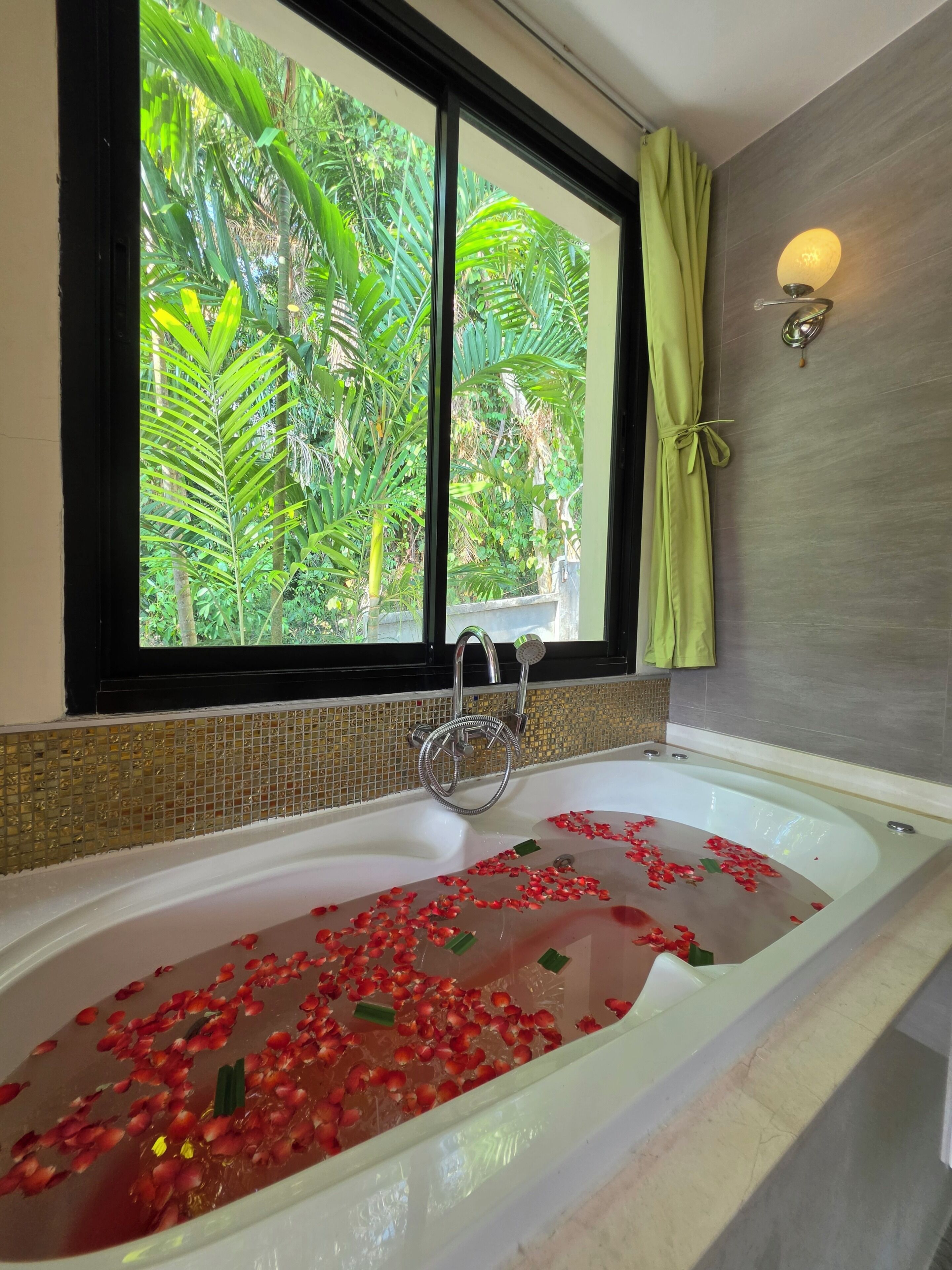 A bathtub with rose petals, a window with a view of greenery, and a towel rack with a towel.