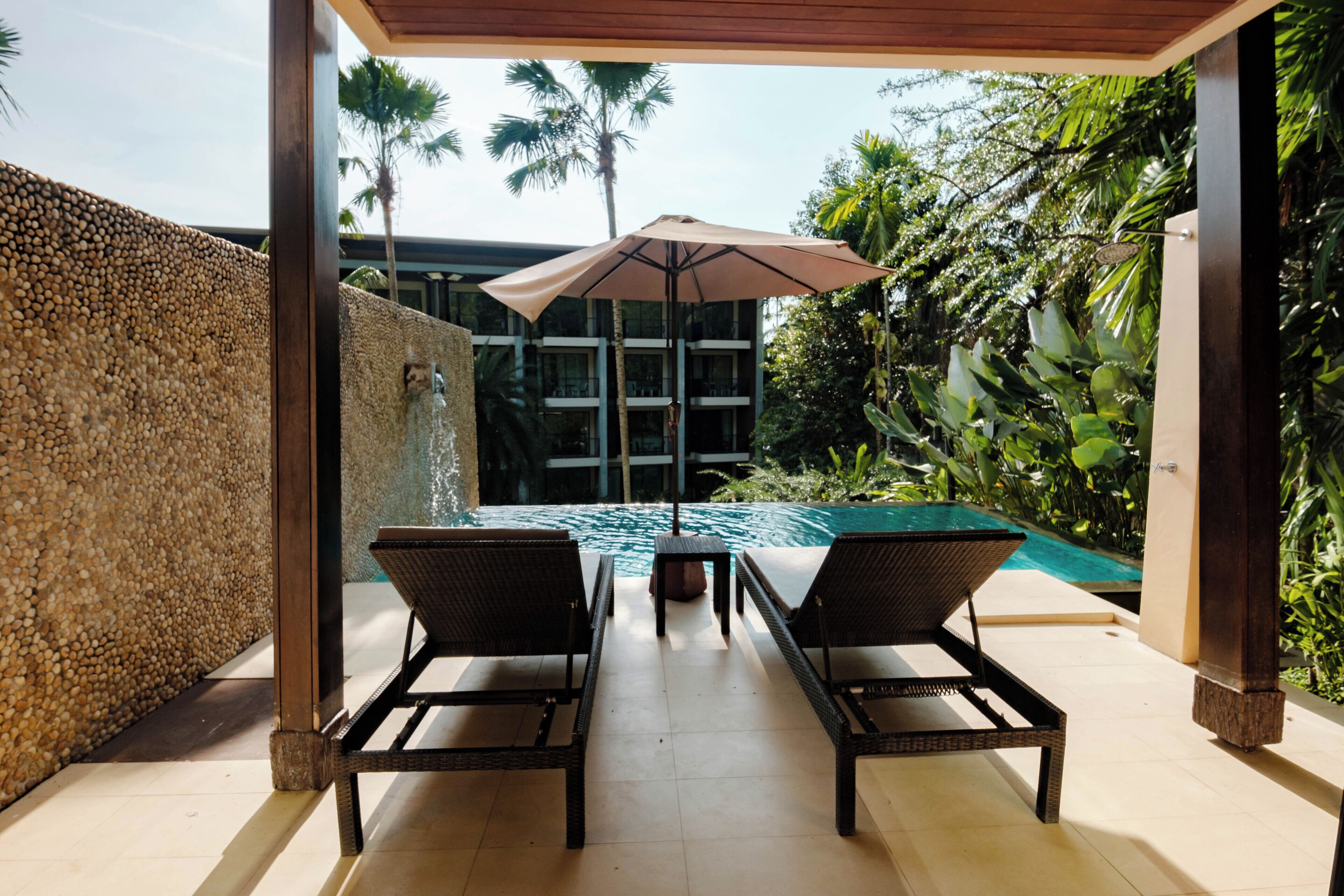 Un área junto a la piscina con dos sillas reclinables, una mesa y una sombrilla.