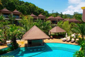 Un resort con piscina, sillones de descanso y construcciones de techo de paja.