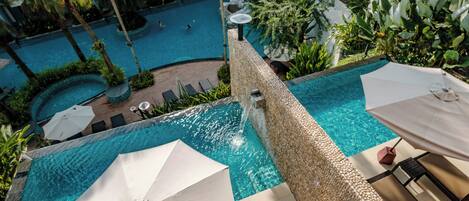 A rooftop pool with clear blue water, surrounded by lush greenery and palm trees.