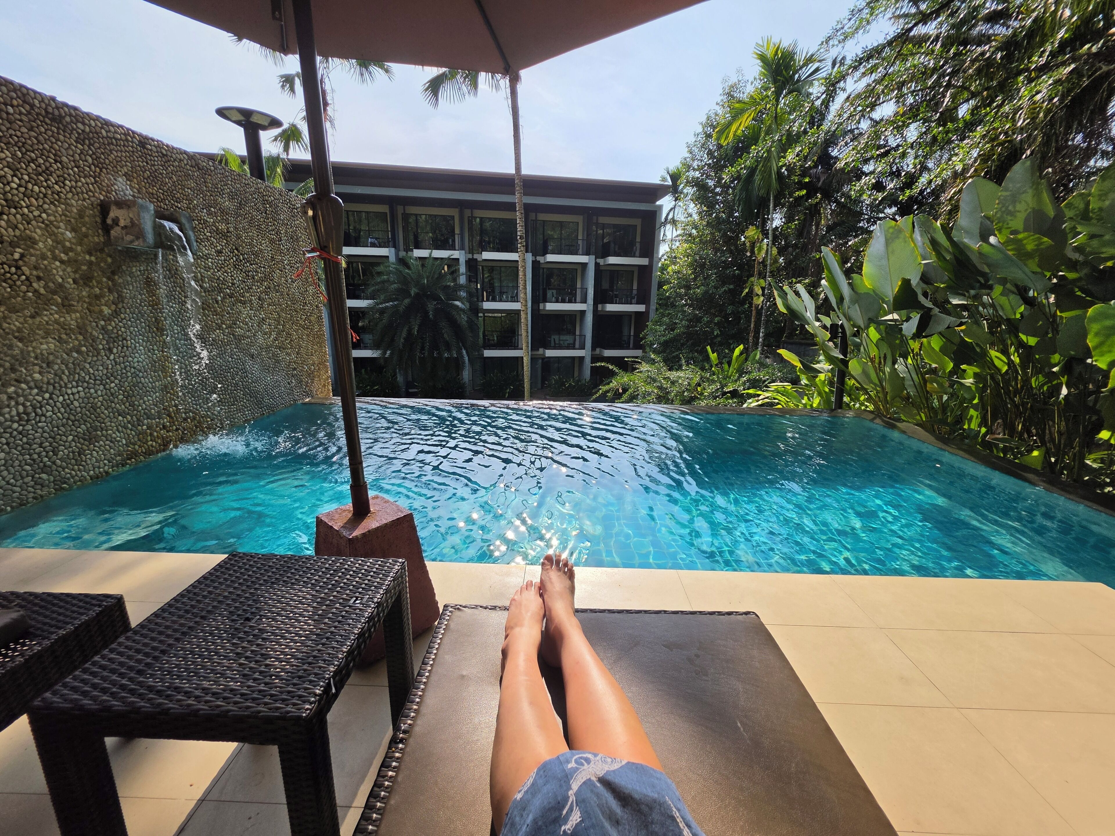 A pool area with a lounge chair, a table, and a building in the background.