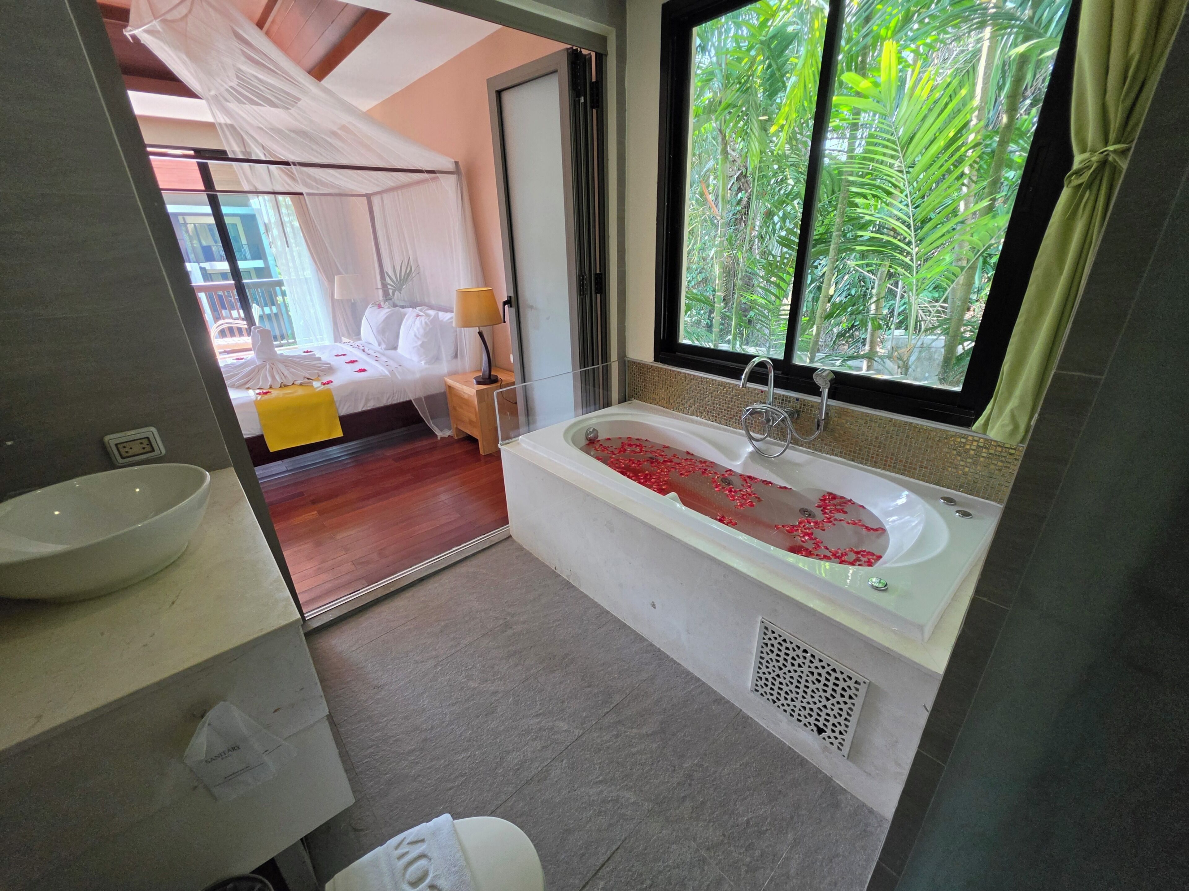 A bathroom with a bathtub, a sink, and a window with a view of greenery.