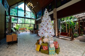 A lobby with a large white Christmas tree surrounded by gift boxes, large windows, and indoor plants.