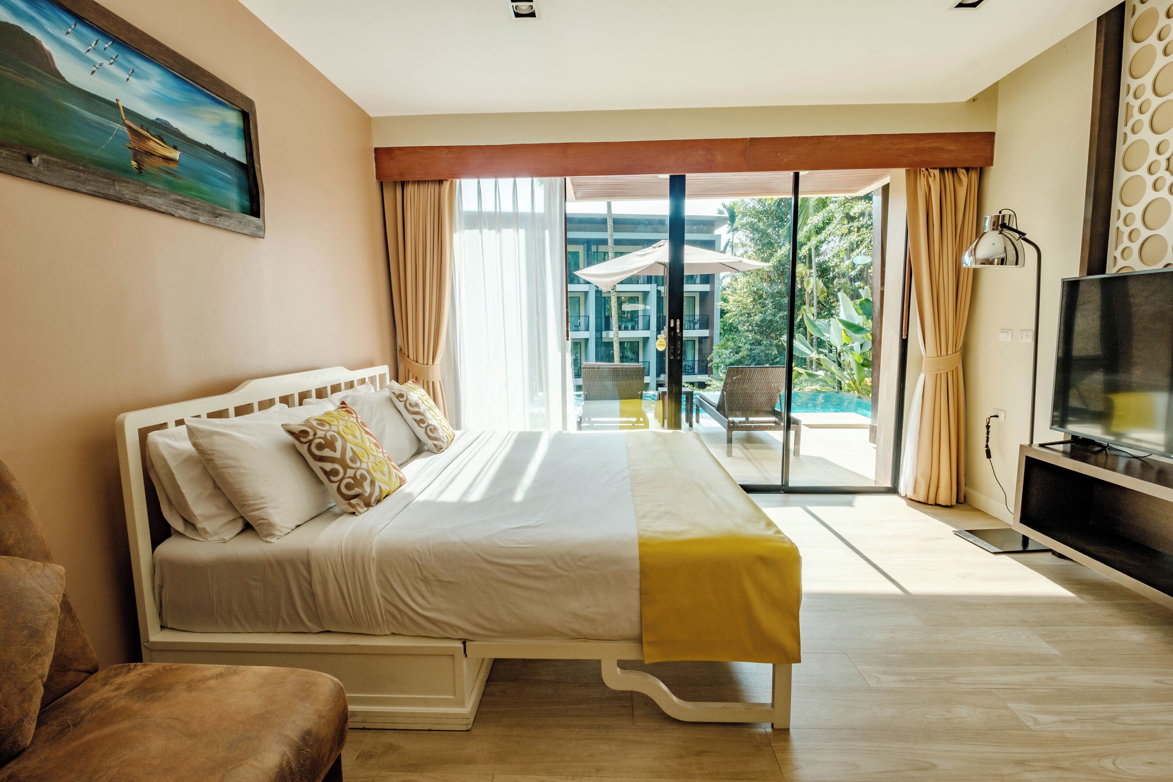 Habitación de hotel con cama, televisión, balcón con cortinas y un cuadro en la pared.
