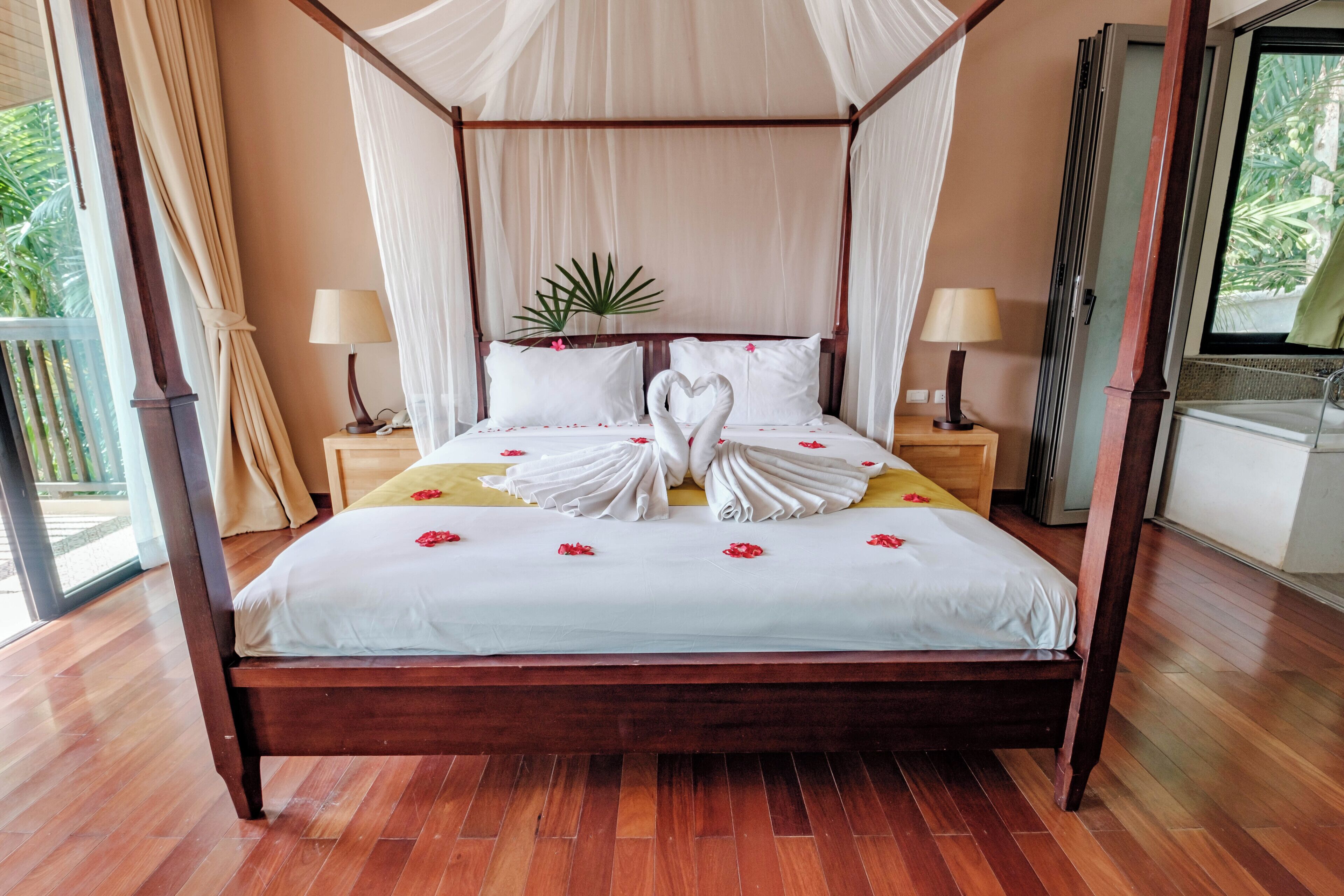 Un lit à baldaquin à quatre poteaux, agrémenté d’une décoration en forme de cœur faite avec des serviettes, de lampes de chevet et d’une plante en pot.