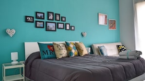 Une chambre avec des murs de couleur turquoise, un lit agrémenté de plusieurs coussins, une table de chevet avec une lampe et des tableaux encadrés accrochés au mur.