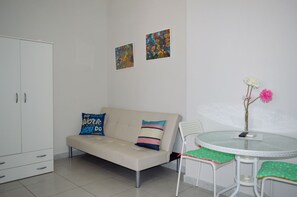A modern living room with a beige sofa, two pillows, a small round table with a vase of flowers, a white cabinet, and two abstract paintings on the wall. - Nel Cuore di Parthenope (Naples)