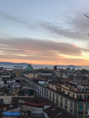 A cityscape with a prominent green dome building, dense urban architecture, and a sunset over the water. - Nel Cuore di Parthenope (Naples)