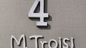 Un panneau avec le chiffre 4 et le nom « M. Troisi » sur un fond texturé.