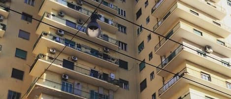 Un edificio residencial de varios pisos con balcones, unidades de aire acondicionado y un cielo azul despejado.