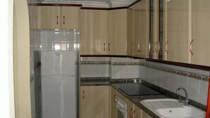 A compact kitchen with beige cabinets, a white refrigerator, a granite countertop, and a sink. - Isla Grosa Apartamentos (San Javier)