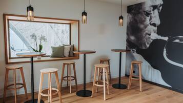 Un interior moderno con piso de madera, mesas redondas y taburetes. Se observa un ventanal con vistas a un paisaje urbano.