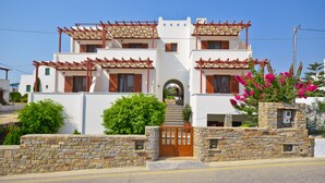 A modern two-story building with a stone wall entrance, wooden shutters, and a pergola. - Anthi Studios (Naxos)